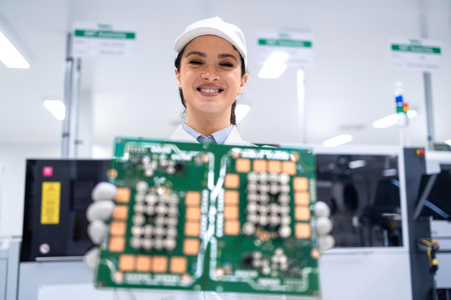 Electronics manufacturing technician holding a printed circuit board near inspection equipment