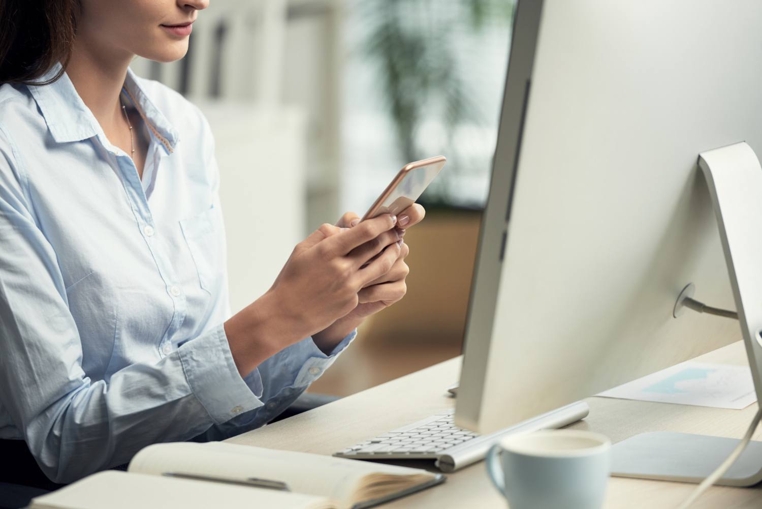 Professional checking business information on a smartphone at a desktop computer