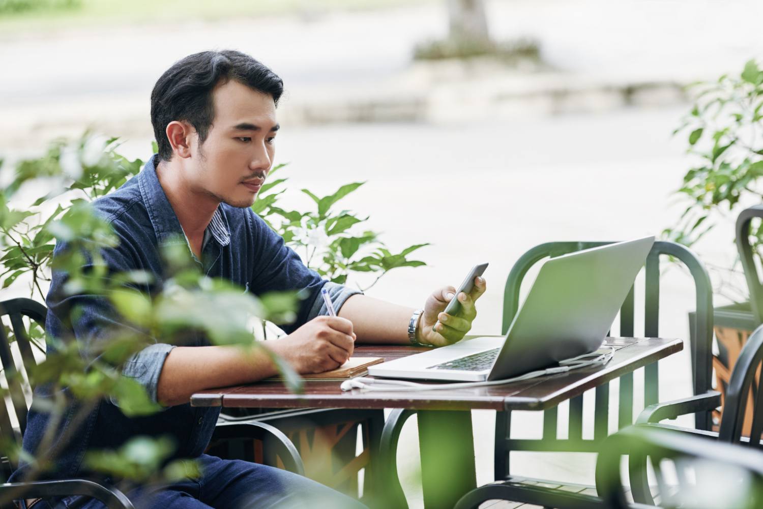 Business owner using a smartphone beside a laptop in a local cafe setting